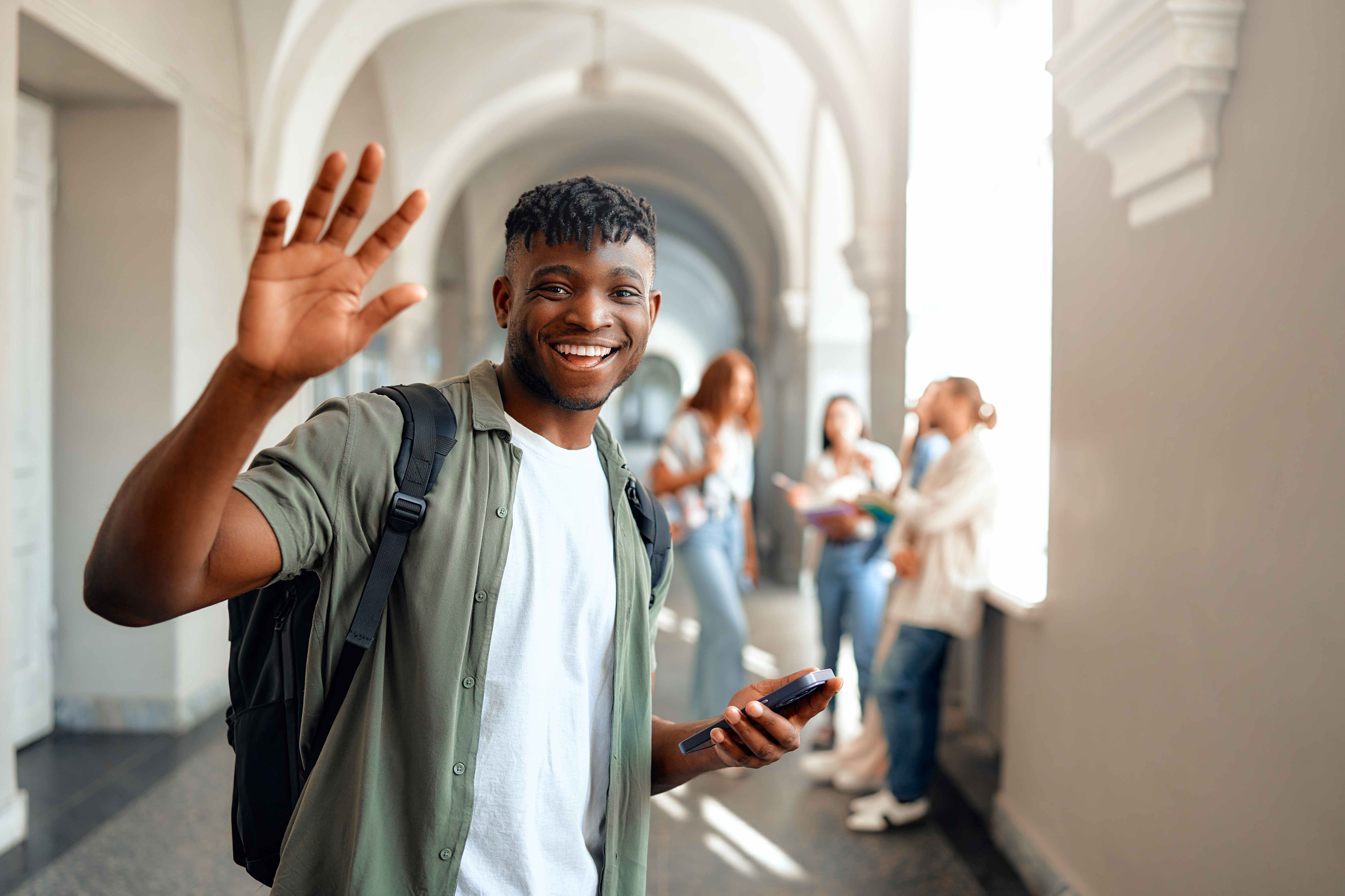 Smiling student waving with friends in a campus hallway